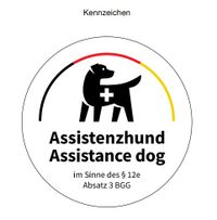 Ein in schwarz gezeichneter Hund, mit einem weißen Kreuz auf Brusthöhe steht unter den Farben der Deutschlandflagge (schwarz - rot - gold). Unter dem Hund steht Assistenzhund - Assistance dog im Sinne des § 12e Absatz 3 BGG